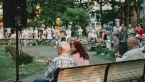 Inimesed istuvad pargis puitpingil ja naudivad vabas õhus toimuvat kontserti suvisel ajal.