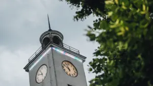 Kõrge kellatorn, mille külgedel on kaks suurt valge sihverplaadiga kella ja puulehed esiplaanil.